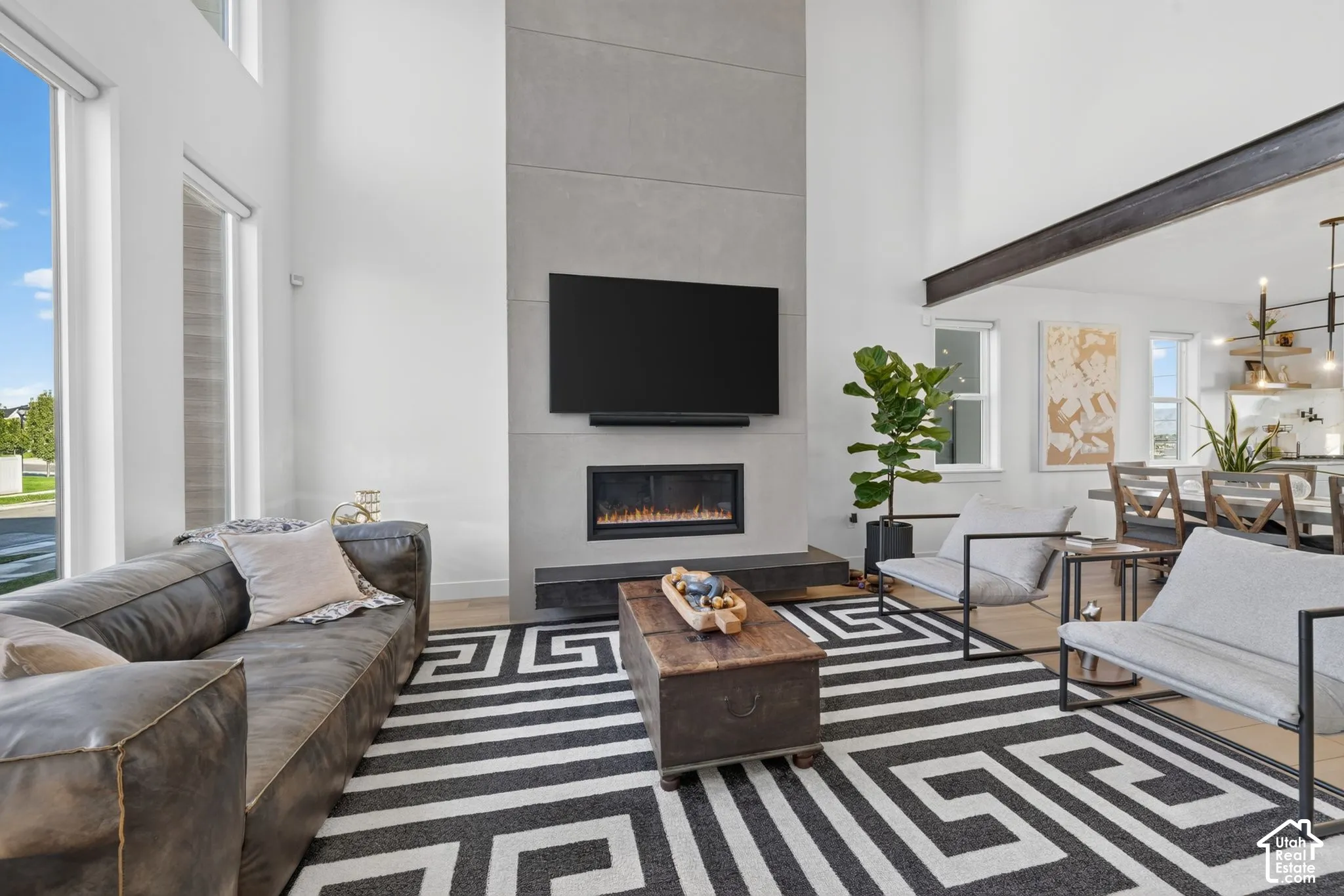 Open-concept living area with a tall, light-toned fireplace feature, an integrated linear electric fireplace, and a high ceiling