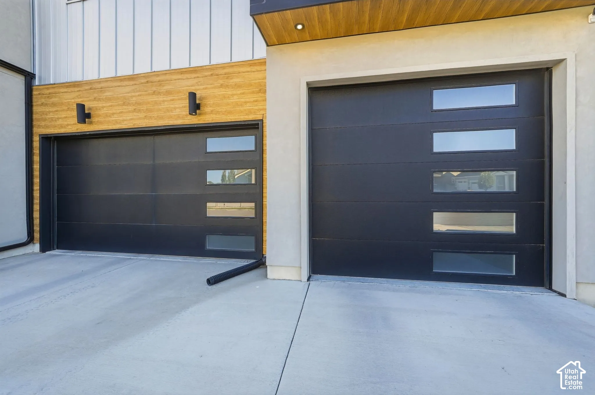Contemporary black garage doors with horizontal window panels, concrete driveway, wood-look exterior siding, and modern wall-mounted light fixtures