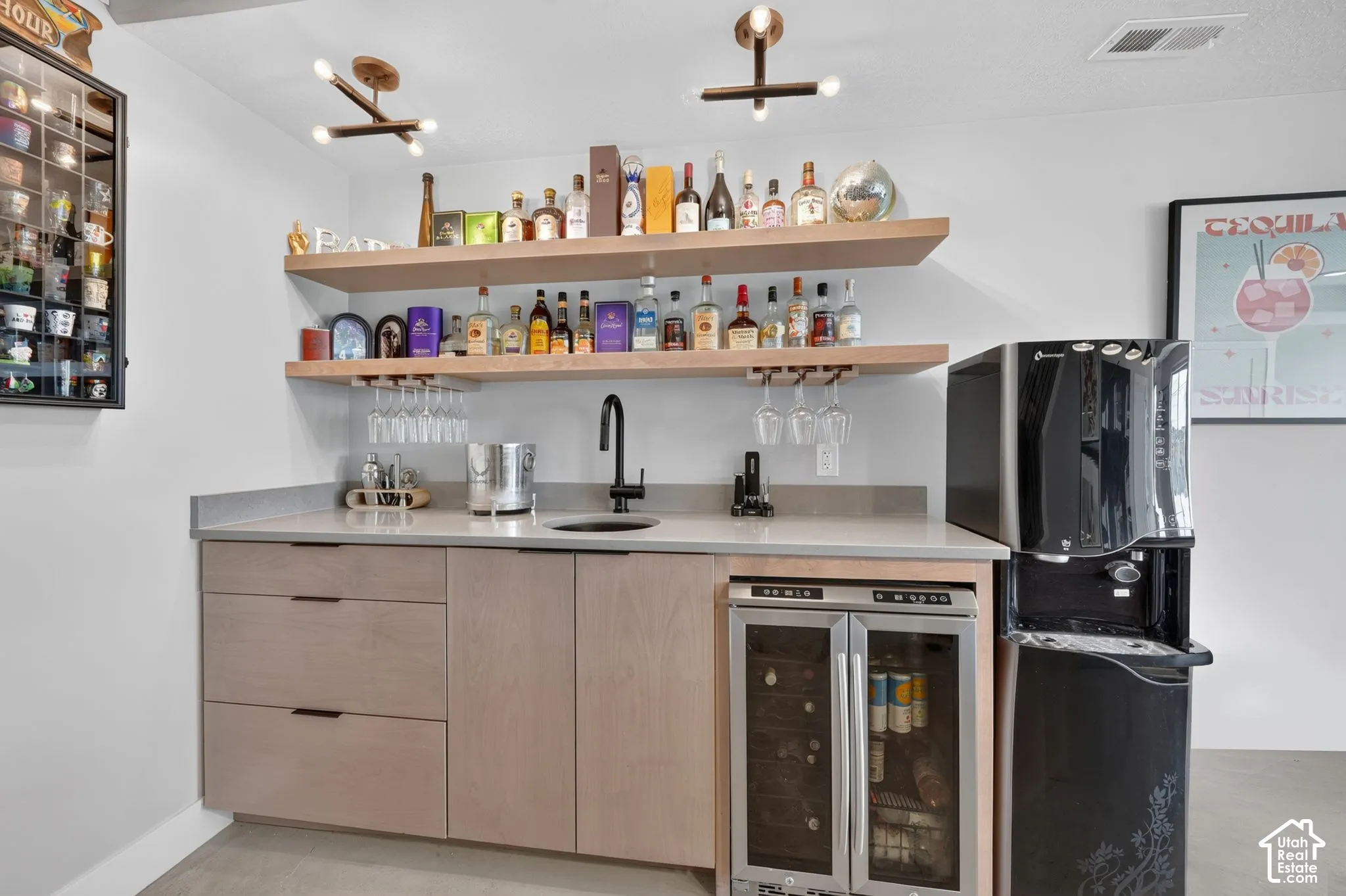 Built-in wet bar featuring a beverage cooler, undermount sink with a matte black faucet, light wood-finish cabinetry, and floating shelves