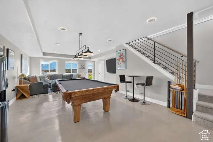 Recessed lighting, wood-finish flooring, staircase with metal railings, multiple windows, and a multi-light pendant fixture