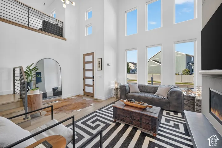 Double-height living space featuring expansive windows, wood-finish flooring, a modern fireplace with a stone-finish surround, and a second-level open railing overlooking the area