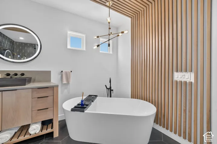 Freestanding bathtub, wood-slat wall feature, dual windows, modern chandelier, and circular illuminated mirror