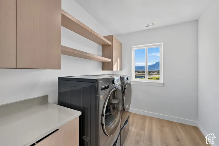 Laundry area featuring wood-finish flooring, light wood cabinetry, open shelving, a light-toned countertop, and a window providing natural illumination