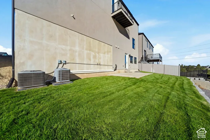 Expansive grassy area with a concrete patio, a privacy fence, and a black metal balcony with railings