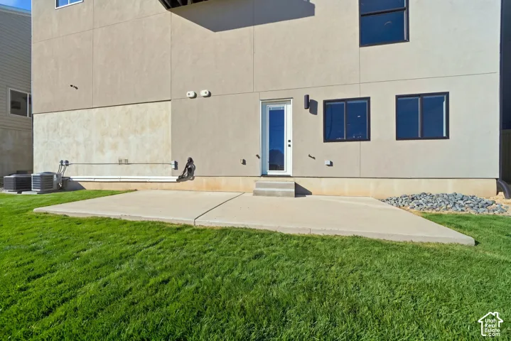 Expansive concrete patio with a walk-out entry and steps, bordered by a manicured lawn