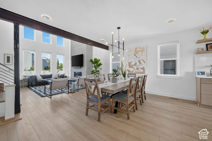 Open-concept interior featuring wood-finish flooring, a contemporary chandelier, recessed lighting, and a living area with a fireplace and tall windows