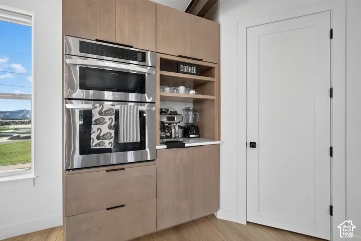 Integrated stainless steel double oven, light wood-finish cabinetry, built-in shelving, white countertop, and a white interior door with black hardware
