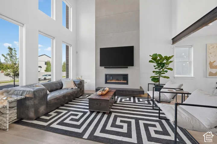Soaring ceilings with extensive window fenestration, wood-finish flooring, a modern fireplace, and a light gray tile accent wall