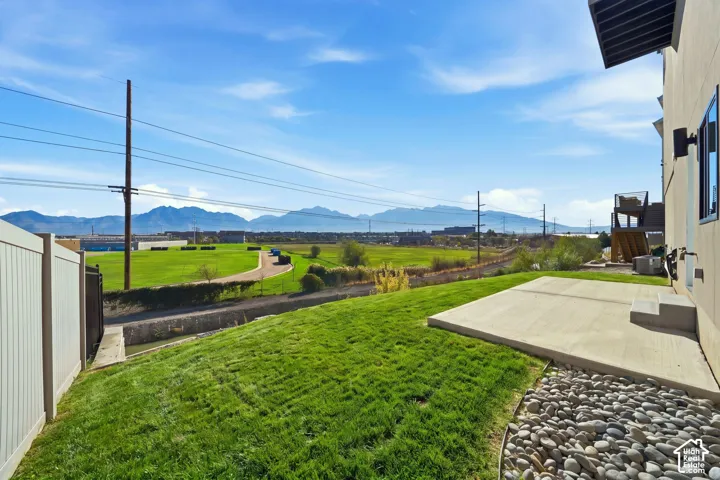 Expansive green lawn, concrete patio, decorative river rock landscaping, and mountain backdrop