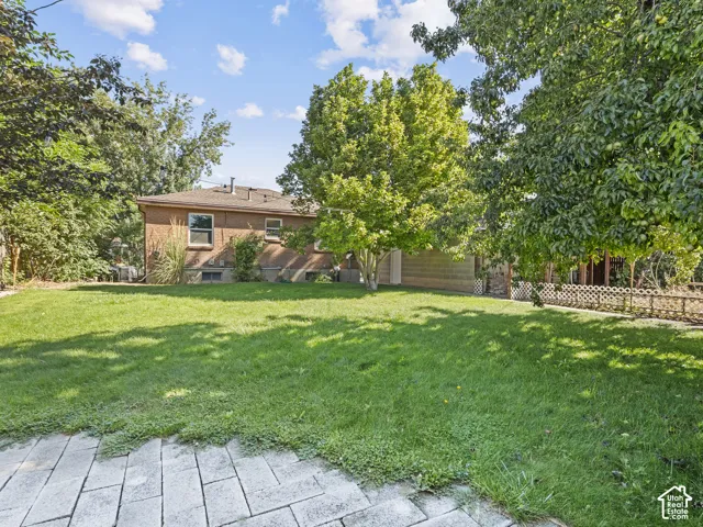 Expansive green lawn framed by mature trees, featuring a brick-clad exterior and a paved patio area