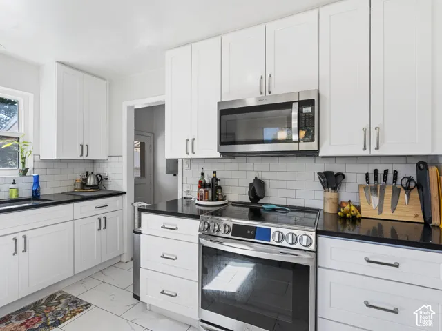 White cabinetry, stainless steel appliances, black countertops, subway tile backsplash, and tile flooring