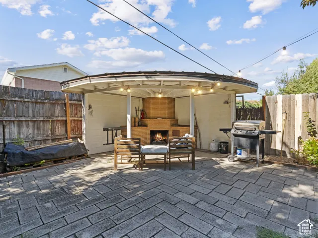 Paved patio featuring a curved covered structure with string lights, and a built-in brick fireplace
