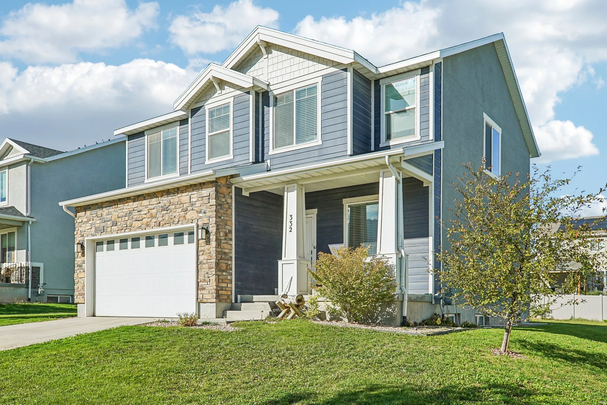 Two-story residence featuring a stone veneer garage with a white sectional door, blue siding, white trim, and a covered porch with white pillars