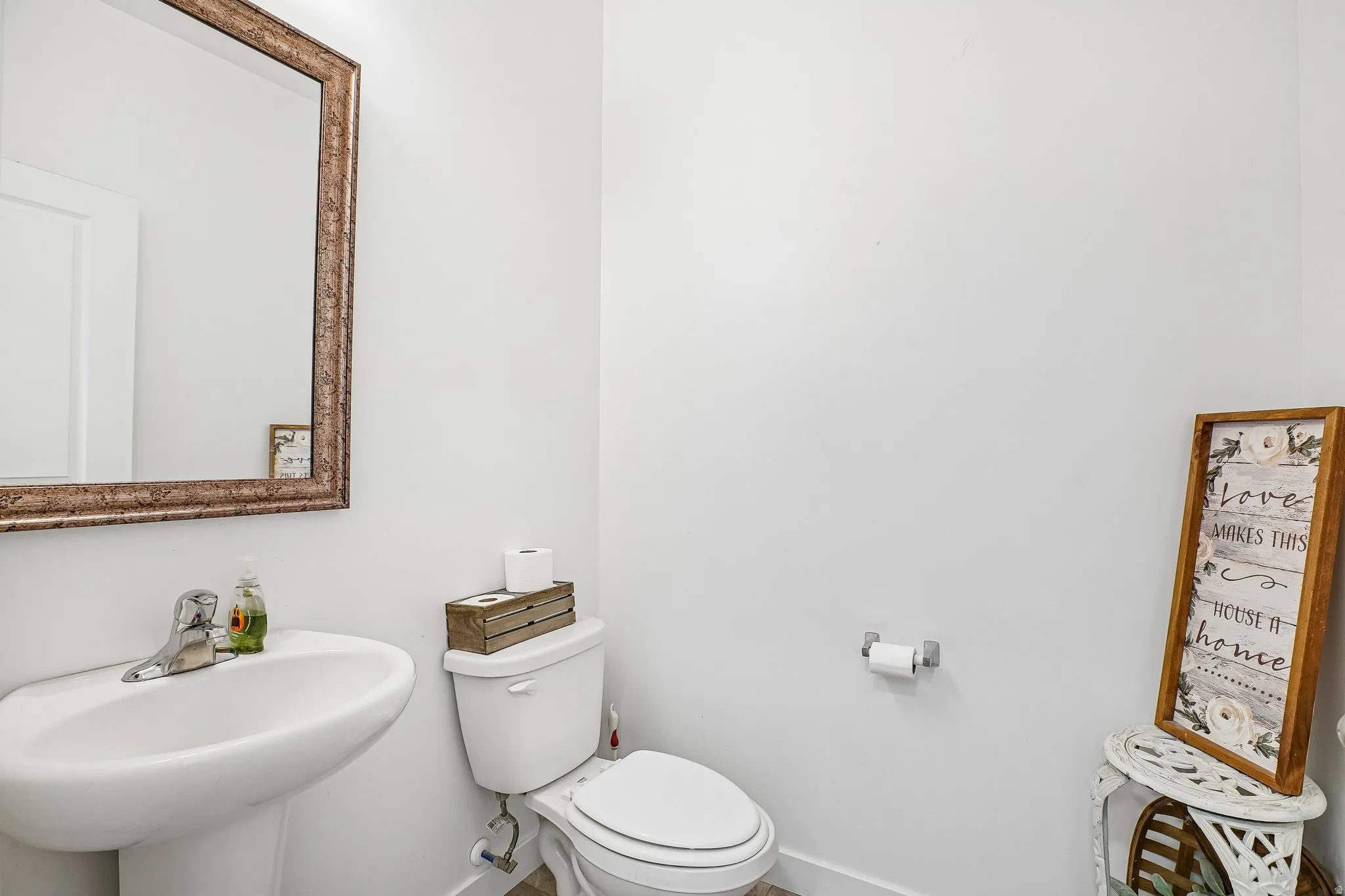 Pedestal sink with a chrome faucet, toilet, and an ornate framed mirror