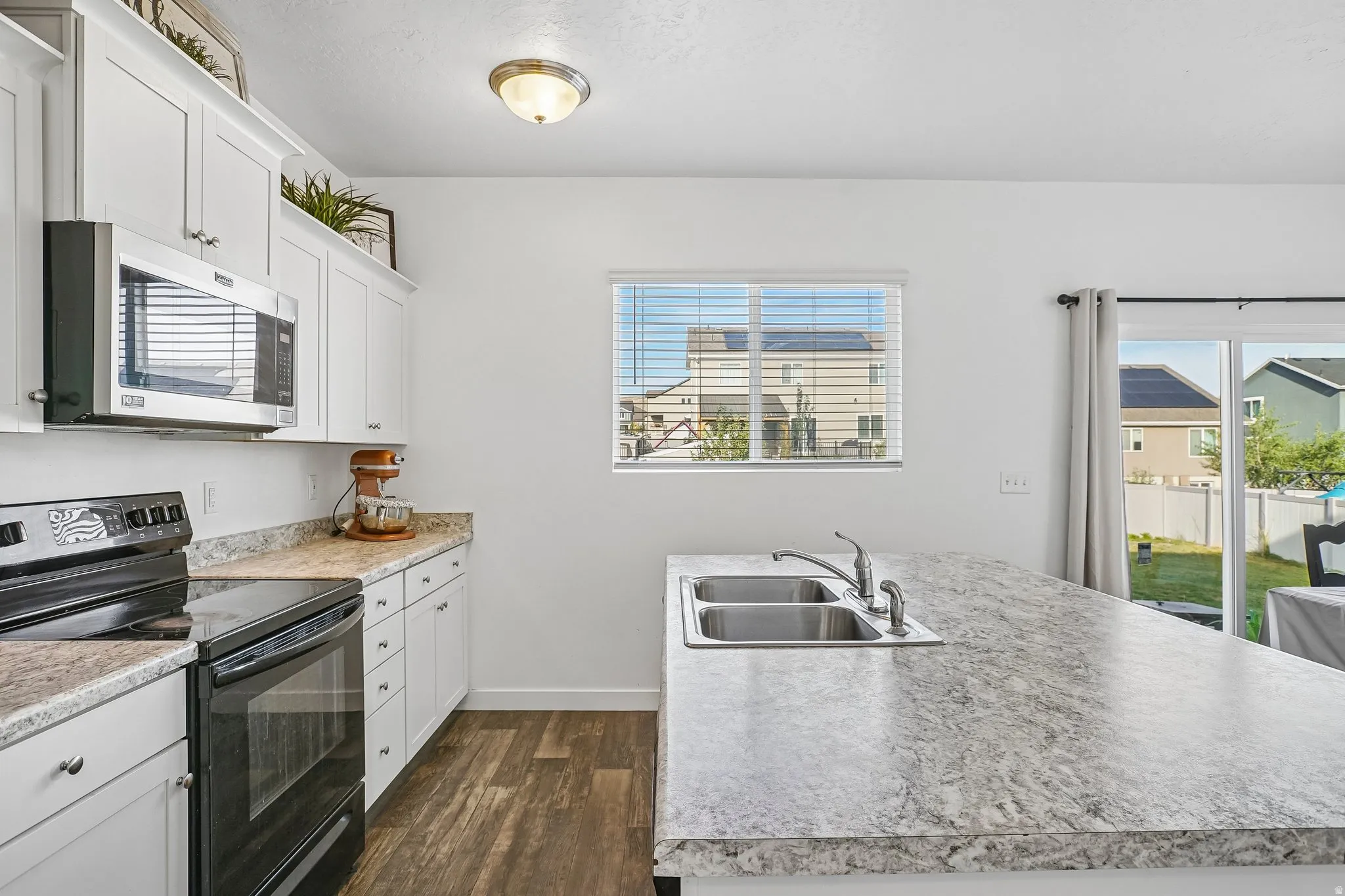 White shaker-style cabinetry, stainless steel microwave, black electric range, dual basin stainless steel sink, and wood-finish flooring
