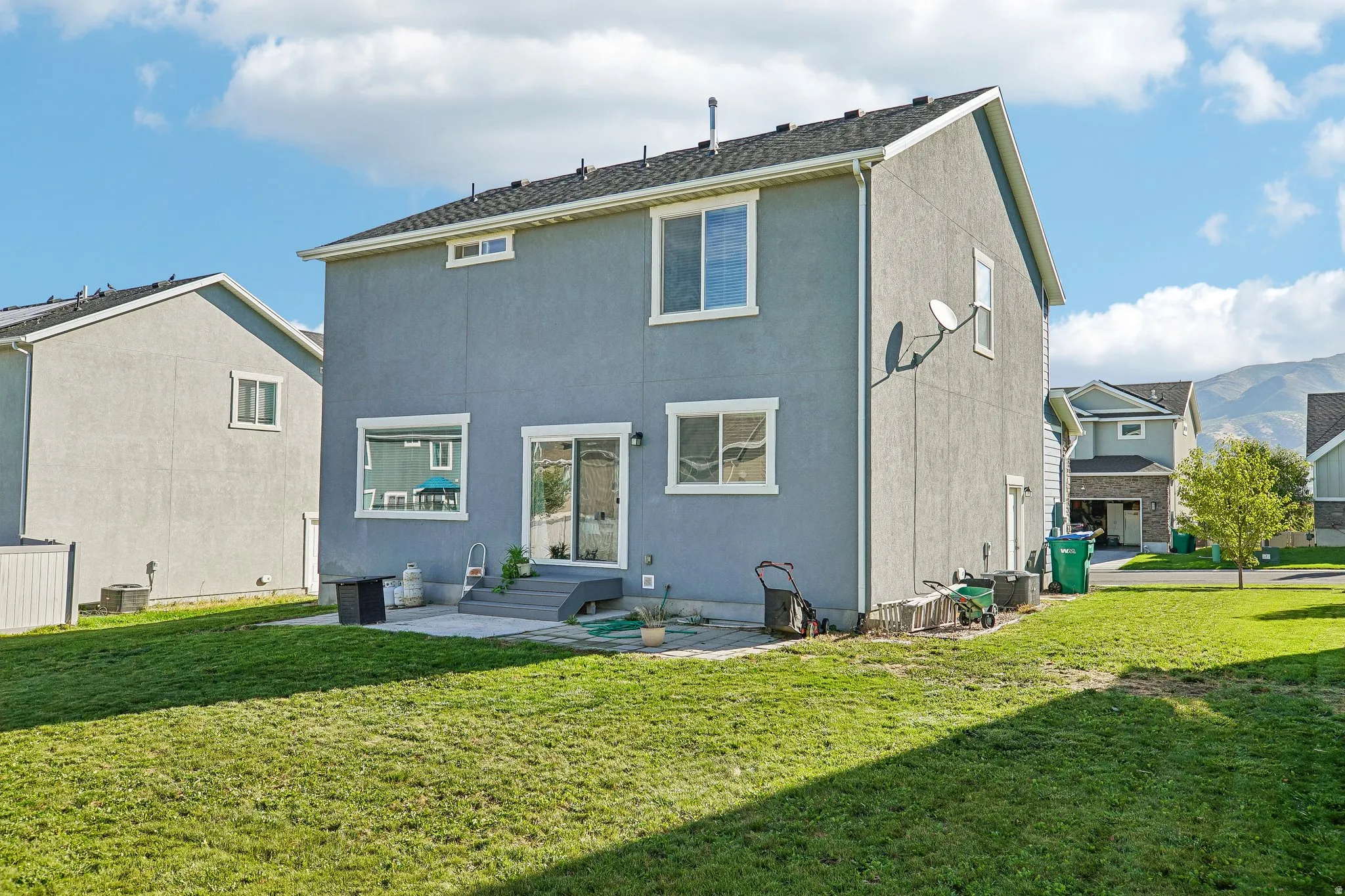 Expansive green lawn with a concrete patio, sliding glass door access, and multiple windows