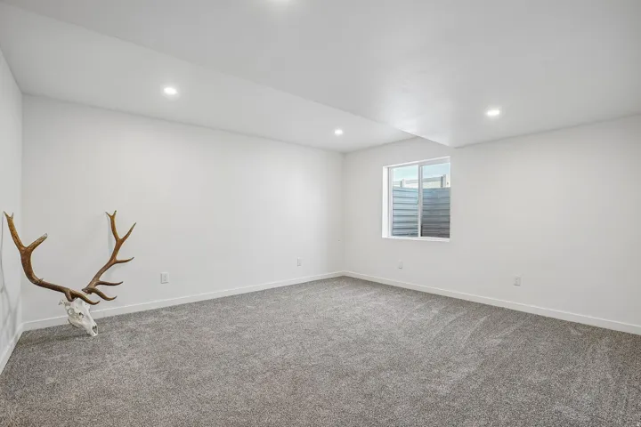 Recessed lighting, light-colored walls, gray carpeting, and a single window with horizontal blinds
