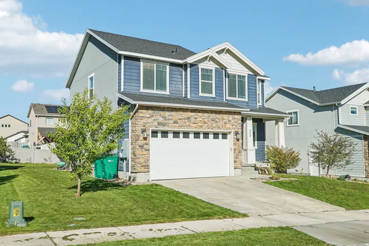 Two-story residence featuring a two-car garage, stone facade accents, blue siding, and a covered entry