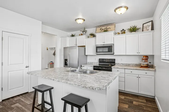 Kitchen featuring a center island with sink, white cabinetry, stainless steel appliances, and wood-finish flooring