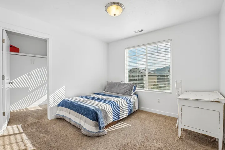 Carpeted room with white walls, a single window with blinds, an overhead light fixture, and an open closet with shelving