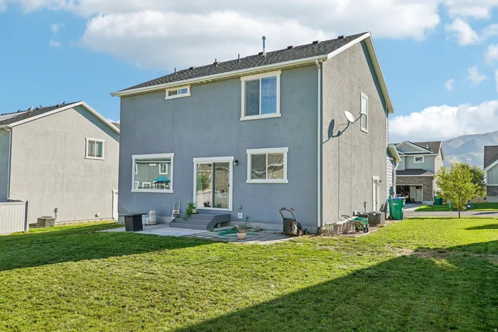 Expansive green lawn with a concrete patio, sliding glass door access, and multiple windows
