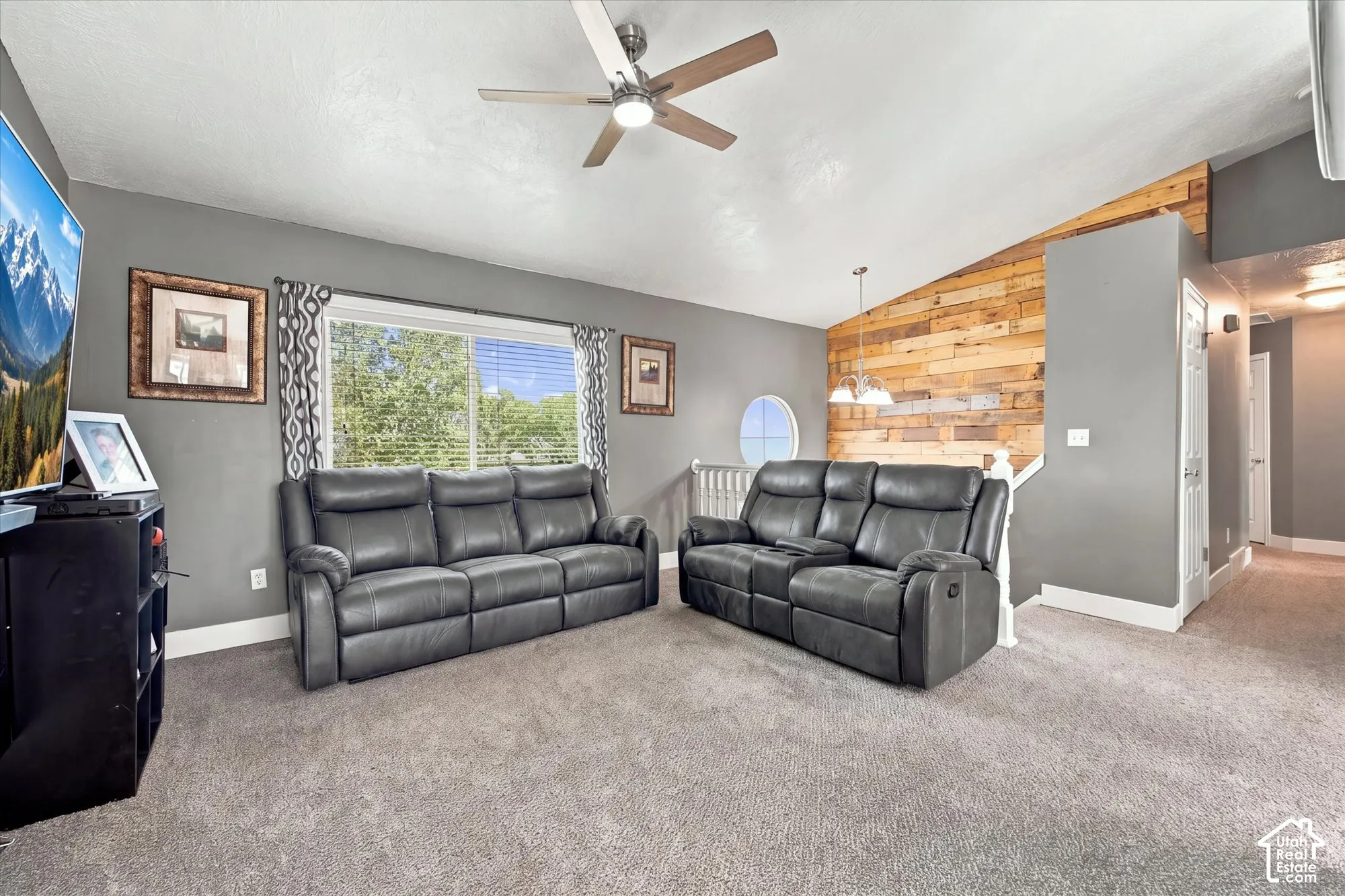 Carpeted floor, wood-paneled accent wall, recessed lighting, ceiling fan with light, and a prominent window