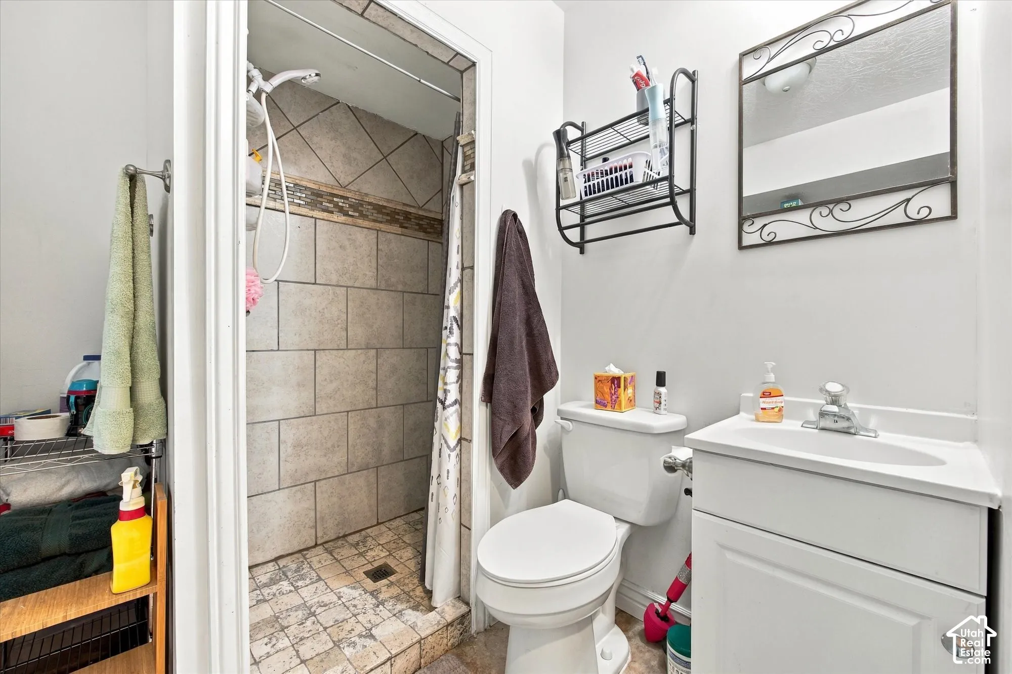 Full bathroom featuring ceramic tile shower surround, white vanity with integrated sink and countertop, toilet, wall-mounted medicine cabinet with mirror, and tile flooring