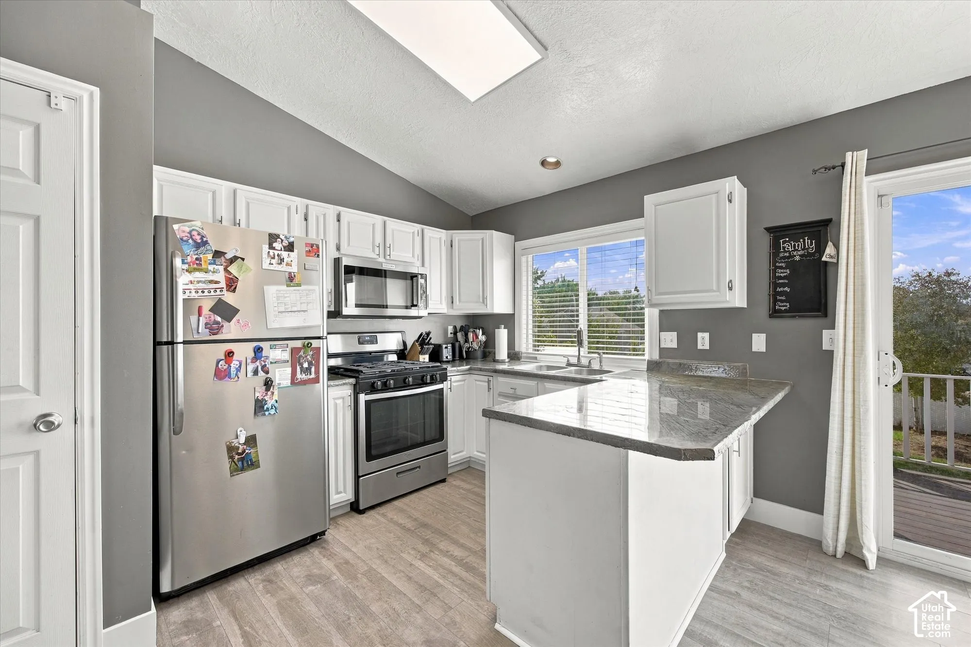 Kitchen featuring white cabinetry, stainless steel appliances, a skylight, wood-finish flooring, and a sliding glass door to exterior