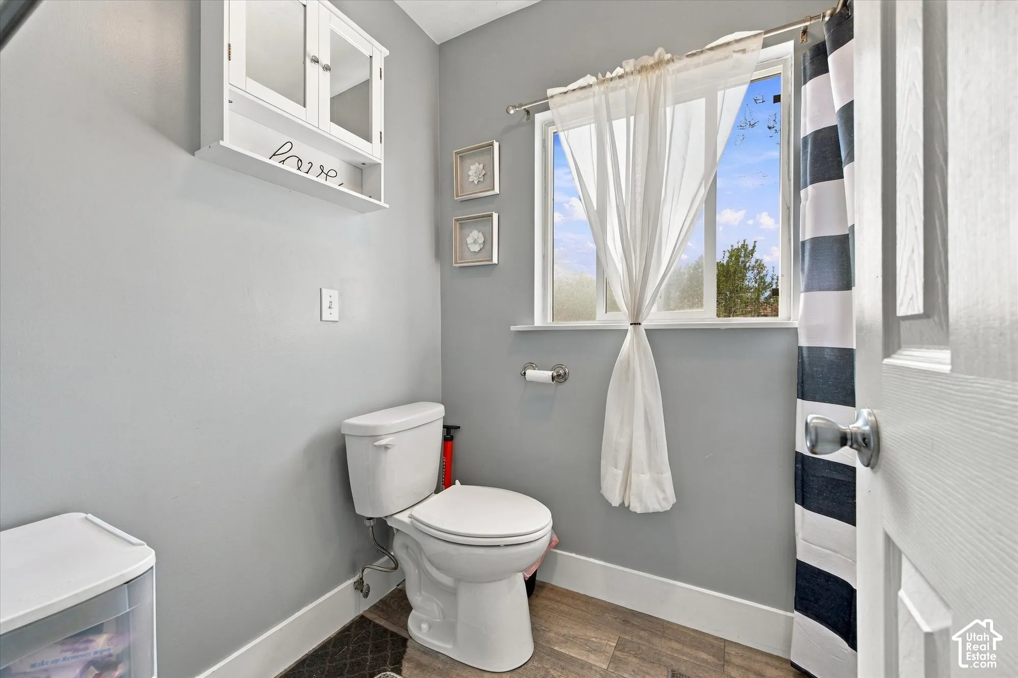 Recessed white storage cabinet, toilet, wood-finish flooring, and a single window