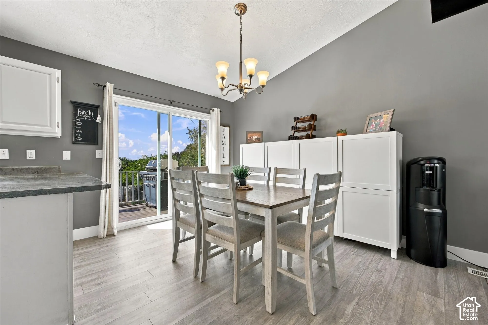 Vaulted ceiling with an attached chandelier, sliding glass door with exterior deck access, light wood-finish flooring, and white cabinetry