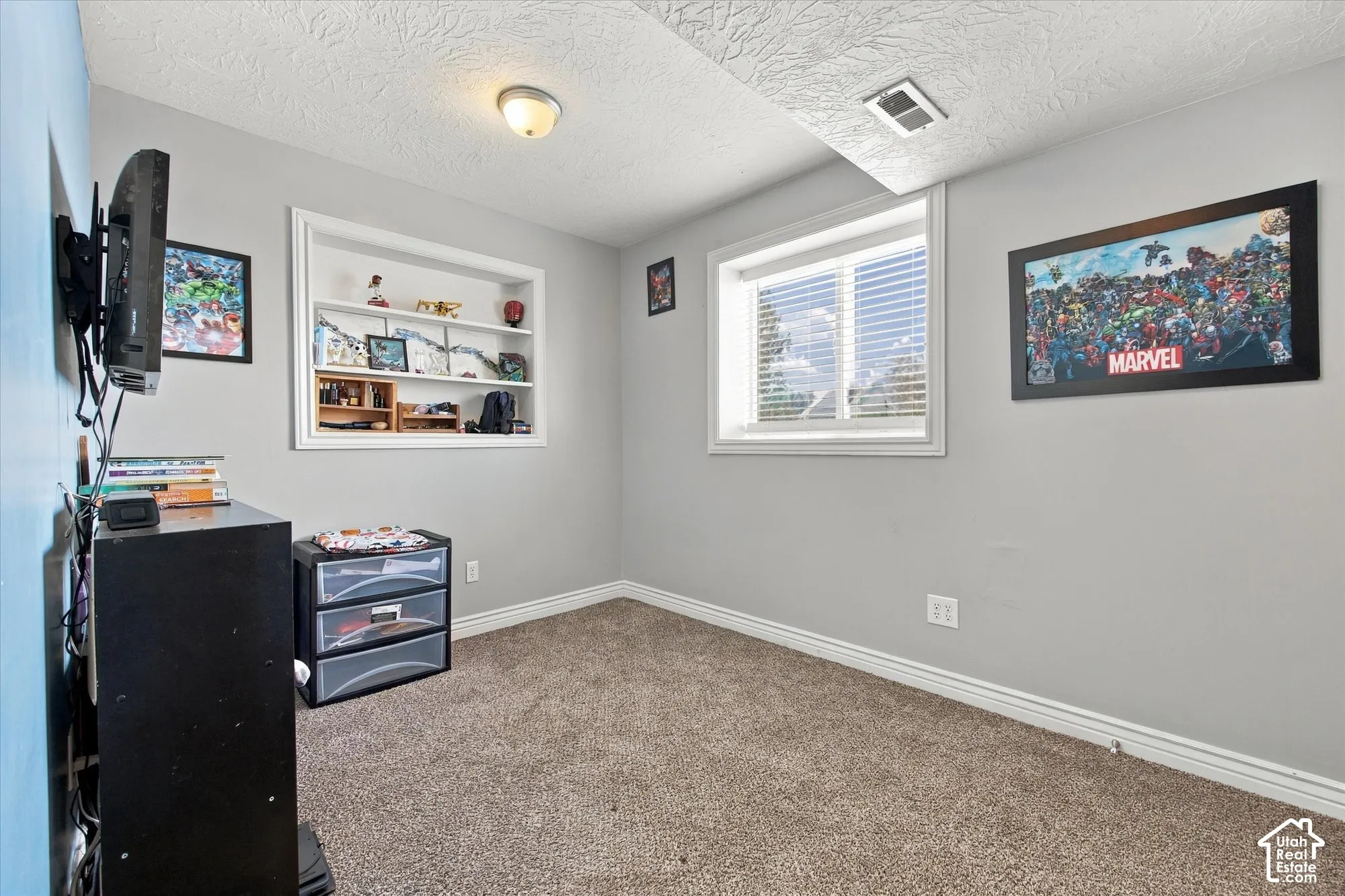 Neutral wall paint, built-in shelving, window with blinds, textured ceiling, and neutral carpet flooring