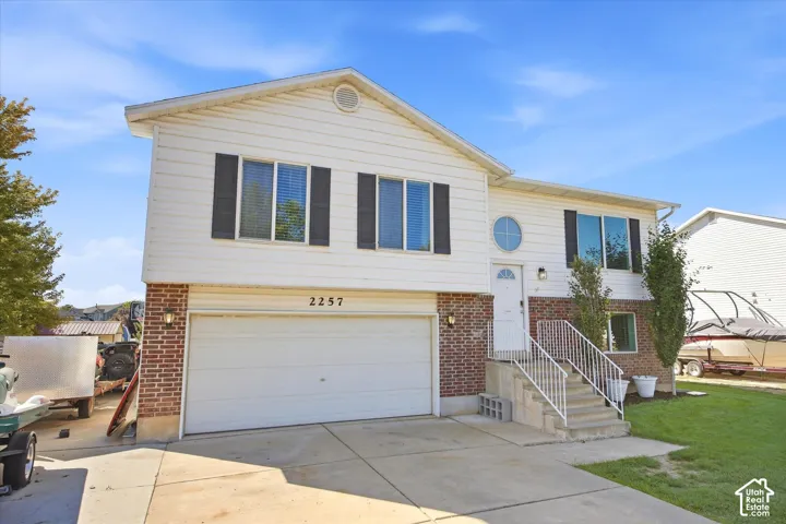 Split-level residence featuring a brick and siding exterior, an attached garage, a front entry staircase with handrails, and a circular window accent