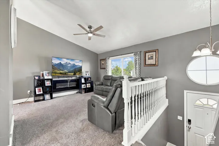 Vaulted ceiling with a ceiling fan, carpeted flooring, large window, white baluster railing, and an oval window