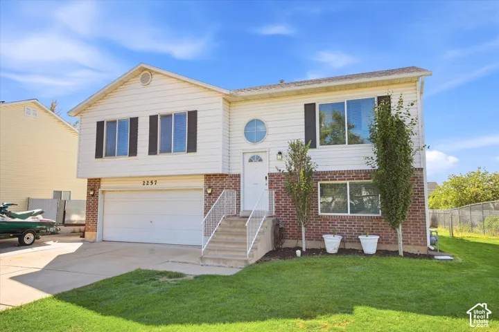 Split-level exterior featuring white siding and brick accents, an integrated garage, and a semicircular window accent