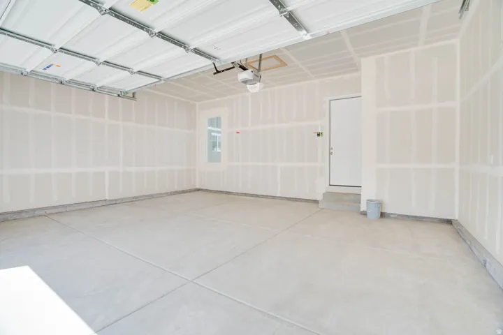 Spacious garage featuring a concrete floor, overhead garage door, interior access door, window, and unfinished drywall walls