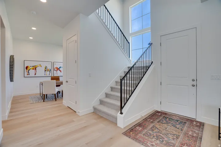 Light wood-finish flooring, recessed ceiling lighting, a staircase with black metal balusters, and a transom window