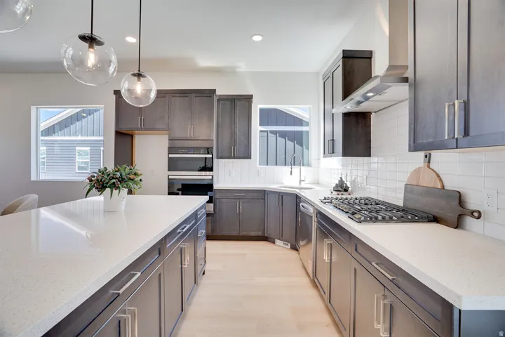 Kitchen featuring an expansive island, light-toned countertops, contrasting dark cabinetry, stainless steel appliances, and wood-finish flooring