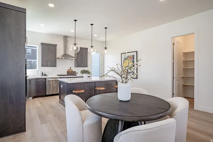 Contemporary kitchen featuring dark wood-finish cabinetry, stainless steel appliances, a center island with seating, pendant lighting, and light wood-finish flooring