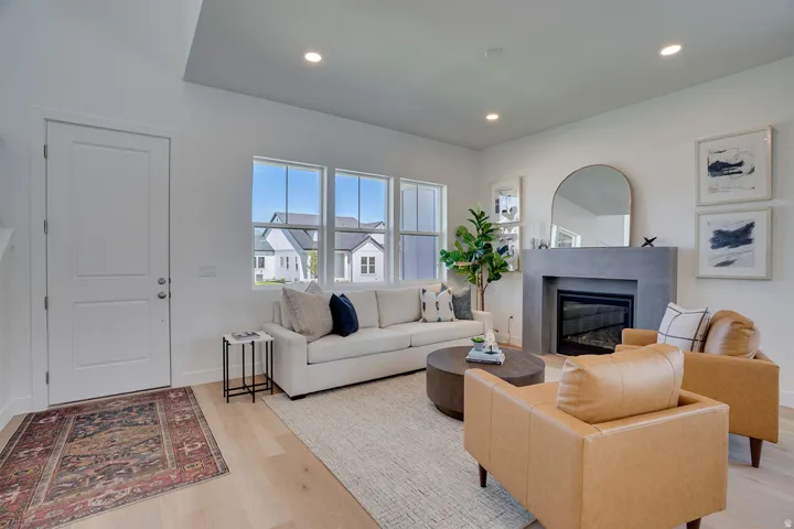 Light wood-finish flooring, a modern fireplace with a stone-look surround, recessed ceiling lighting, and multiple windows with exterior views