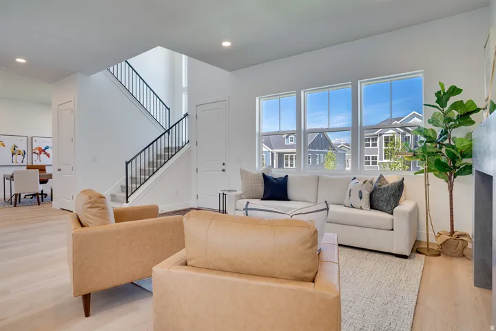 Open-concept interior featuring light wood-finish flooring, a contemporary staircase with black metal railings, recessed lighting, and a wall of three large windows