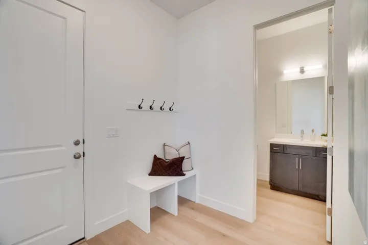 Light wood-finish flooring extending into the hallway, white painted door with brushed nickel hardware, and a wall-mounted coat rack