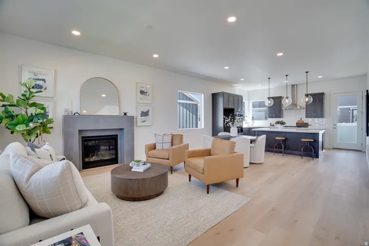 Open-concept living area with wood-finish flooring, a contemporary fireplace, recessed lighting, and a kitchen featuring dark cabinetry and a center island