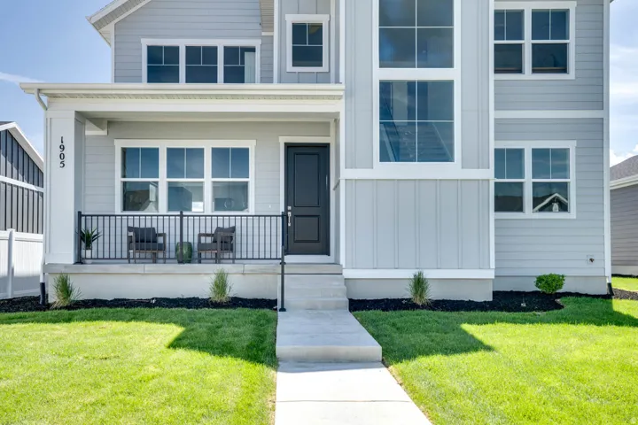 Contemporary exterior with light gray siding, a covered front porch, a contrasting dark entry door, and a prominent multi-story window feature