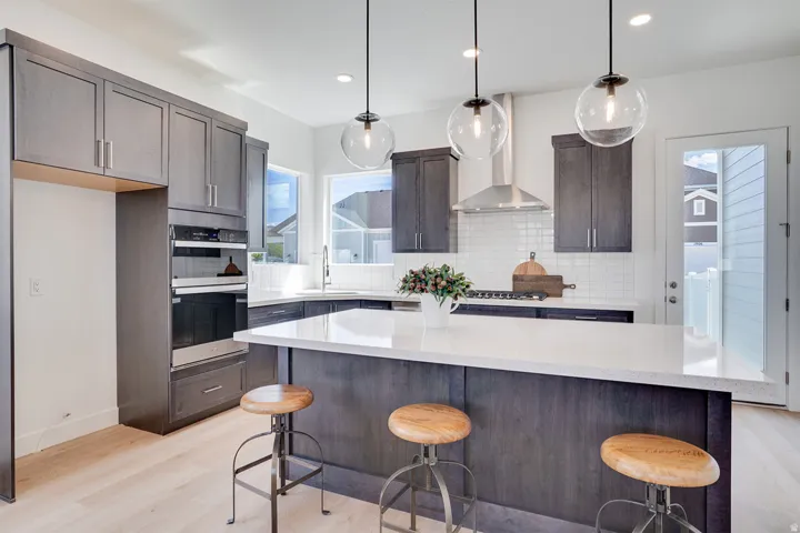 Kitchen featuring wood-finish cabinetry, built-in double ovens, light-toned wood-finish flooring, and a subway tile backsplash