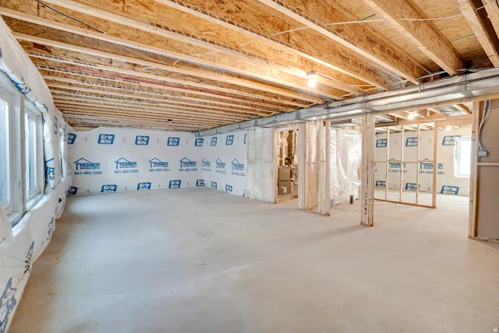 Unfinished basement space featuring exposed wood joists, concrete flooring, multiple windows, and partial framing for future rooms