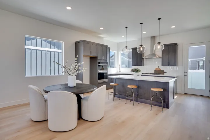 Modern kitchen featuring dark wood-finish cabinetry, a large kitchen island with seating, pendant lighting, built-in stainless steel appliances, and light wood-finish flooring