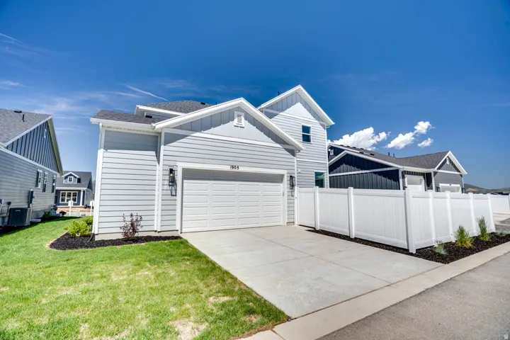 Light grey siding exterior with white trim, attached two-car garage, concrete driveway, white privacy fencing, and a landscaped yard