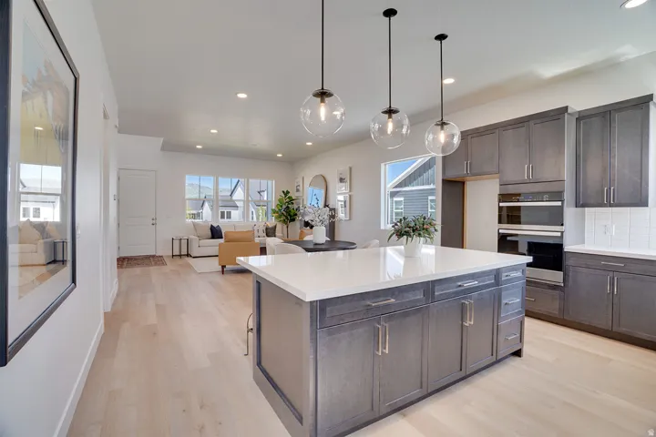 Spacious kitchen island with light-toned countertop, pendant lighting, built-in double ovens, and extensive cabinetry