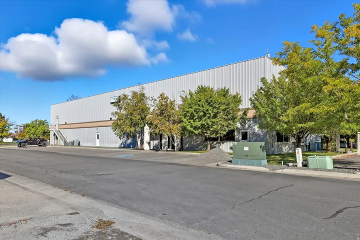 Large industrial building featuring a metal panel exterior, multiple ground-level entrances, and a paved parking area