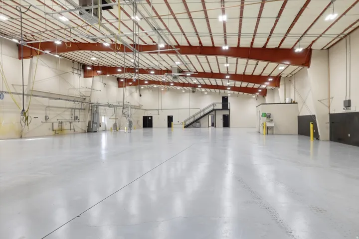 Expansive interior featuring an industrial-style polished concrete floor, exposed structural beams, high ceilings, and a built-in mezzanine with a steel staircase
